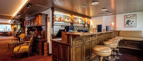A bar area with wooden bar stools, a counter with bottles, and a seating area with a couch.