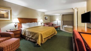 Een hotelkamer met een groot bed, twee nachtkastjes, een bureau, een stoel, een televisie en een badkamerruimte.