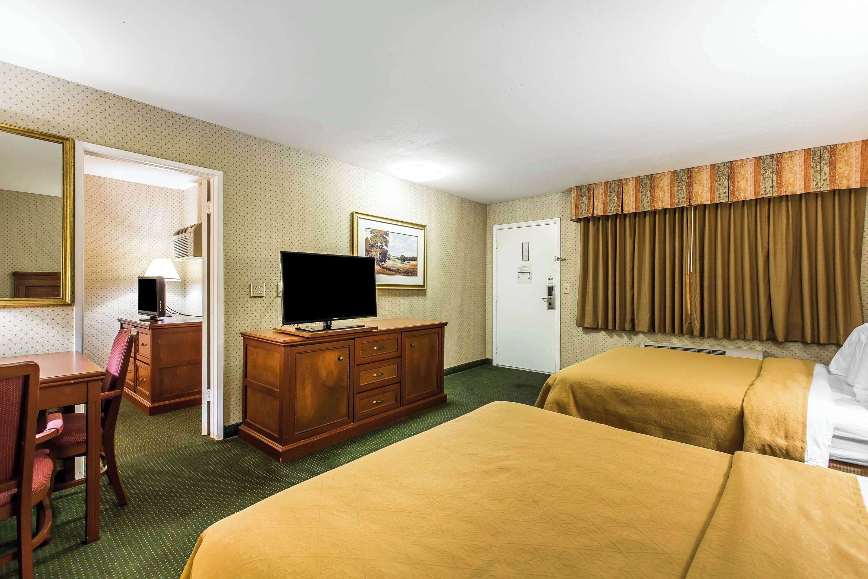 A hotel room with two beds, a desk with a chair, a television, a dresser, and a door.