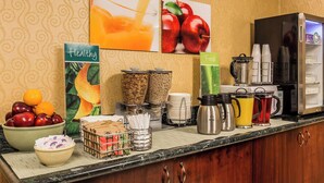 Een ontbijtruimte in een hotel met een fruitschaal, koffiezetapparaat en diverse ontbijtartikelen op het aanrecht.