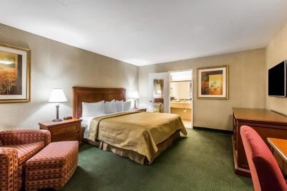 A hotel room with a bed, two bedside tables, a desk, a chair, and a television.