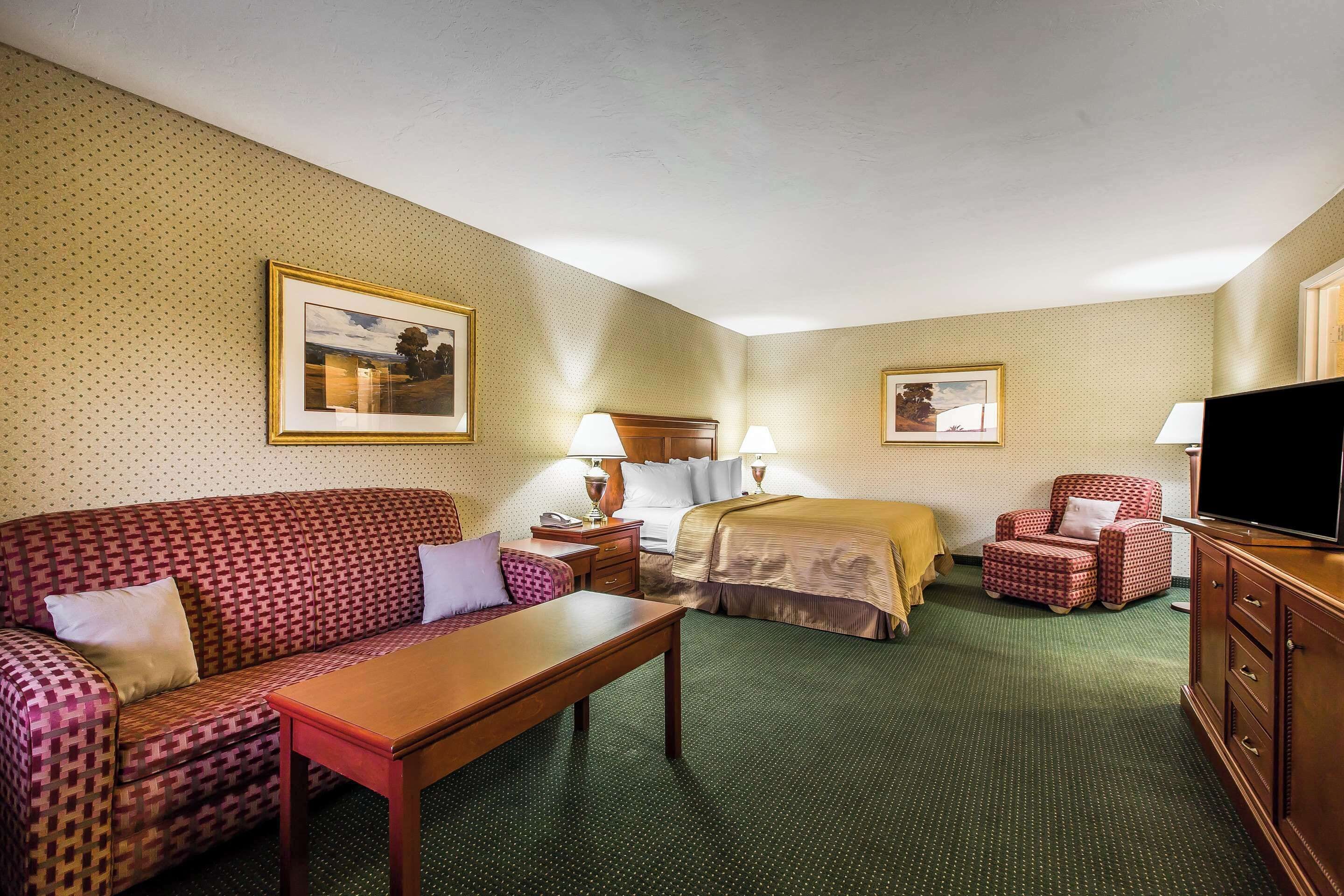A hotel room with a sofa, a bed, a desk, a chair, a TV, and two framed pictures on the wall.
