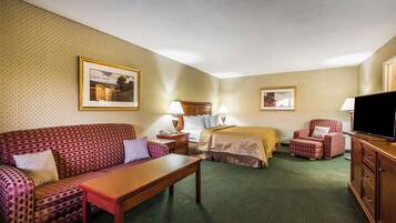 A hotel room with a sofa, a bed, a desk, a chair, a TV, and two framed pictures on the wall.