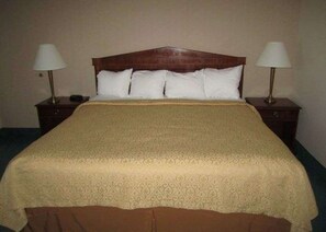 Una habitación de hotel estándar con cabecera de madera, cama con ropa blanca y dos lámparas de noche.