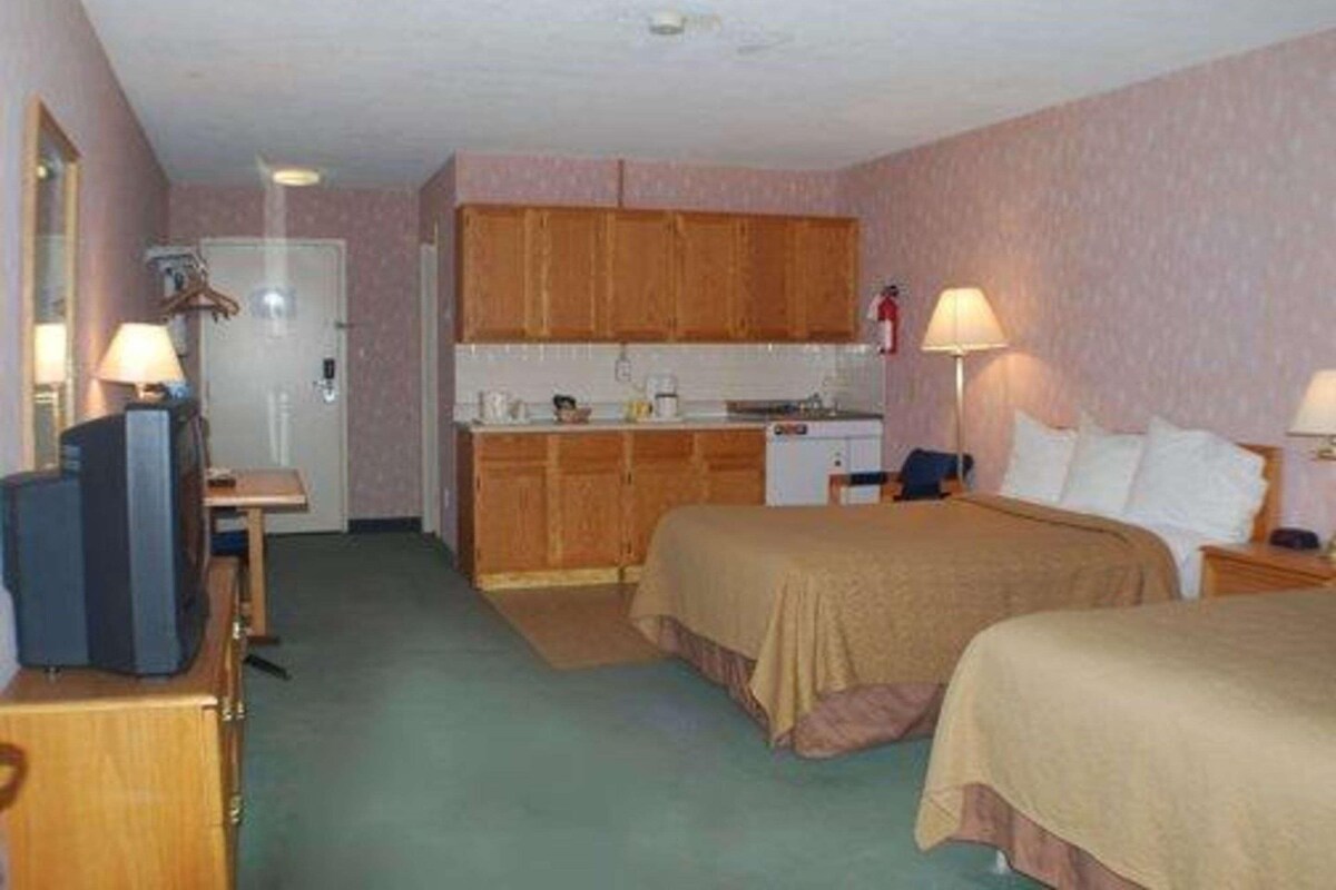 Una habitación de hotel con kitchenette, televisión, cama y mesita de noche.