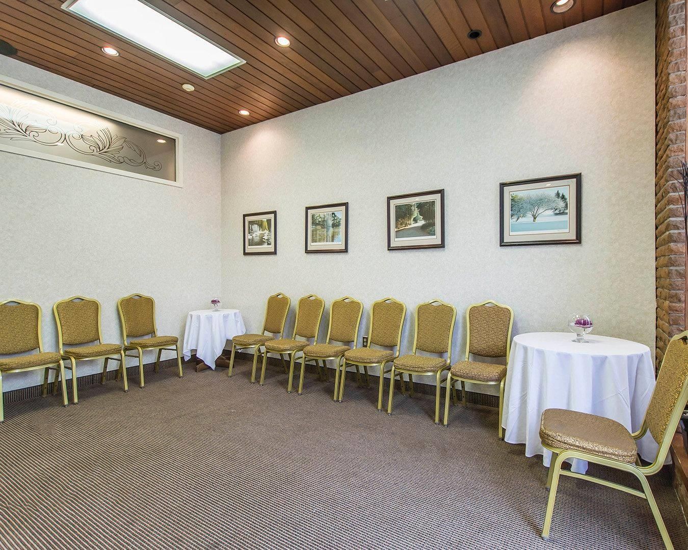 Una sala conferenze con un lungo tavolo e sedie, quadri appesi al muro e pavimento rivestito a moquette.