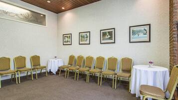 Una sala conferenze con un lungo tavolo e sedie, quadri appesi al muro e pavimento rivestito a moquette.