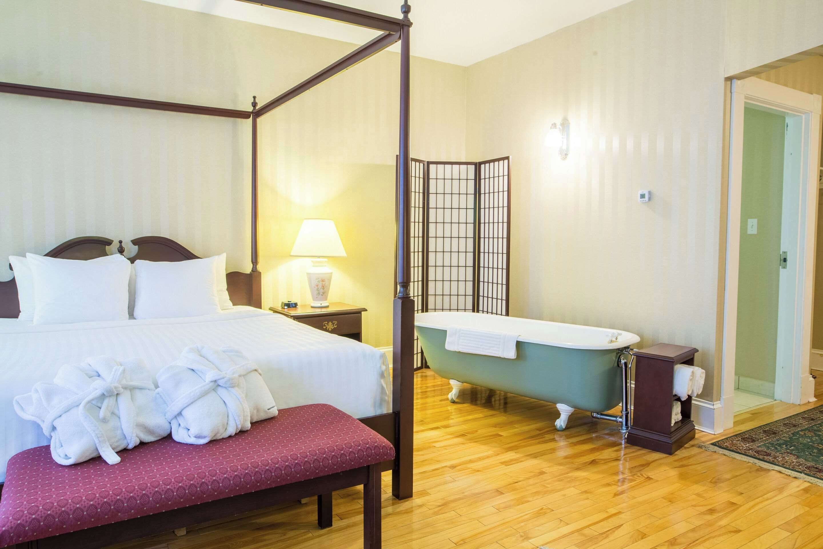 Una cama con dosel, sábanas blancas, una lámpara de noche y un banco de madera con toallas.