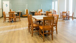 A spacious dining area with wooden tables and chairs, patterned wallpaper, and pendant lighting. - Quality Inn & Suites Downtown (Charlottetown)
