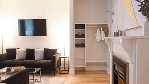 A modern living room with a sofa, coffee table, and a flat-screen TV. There is a fireplace and a closet with shelves. - Quality Inn & Suites Downtown (Charlottetown)
