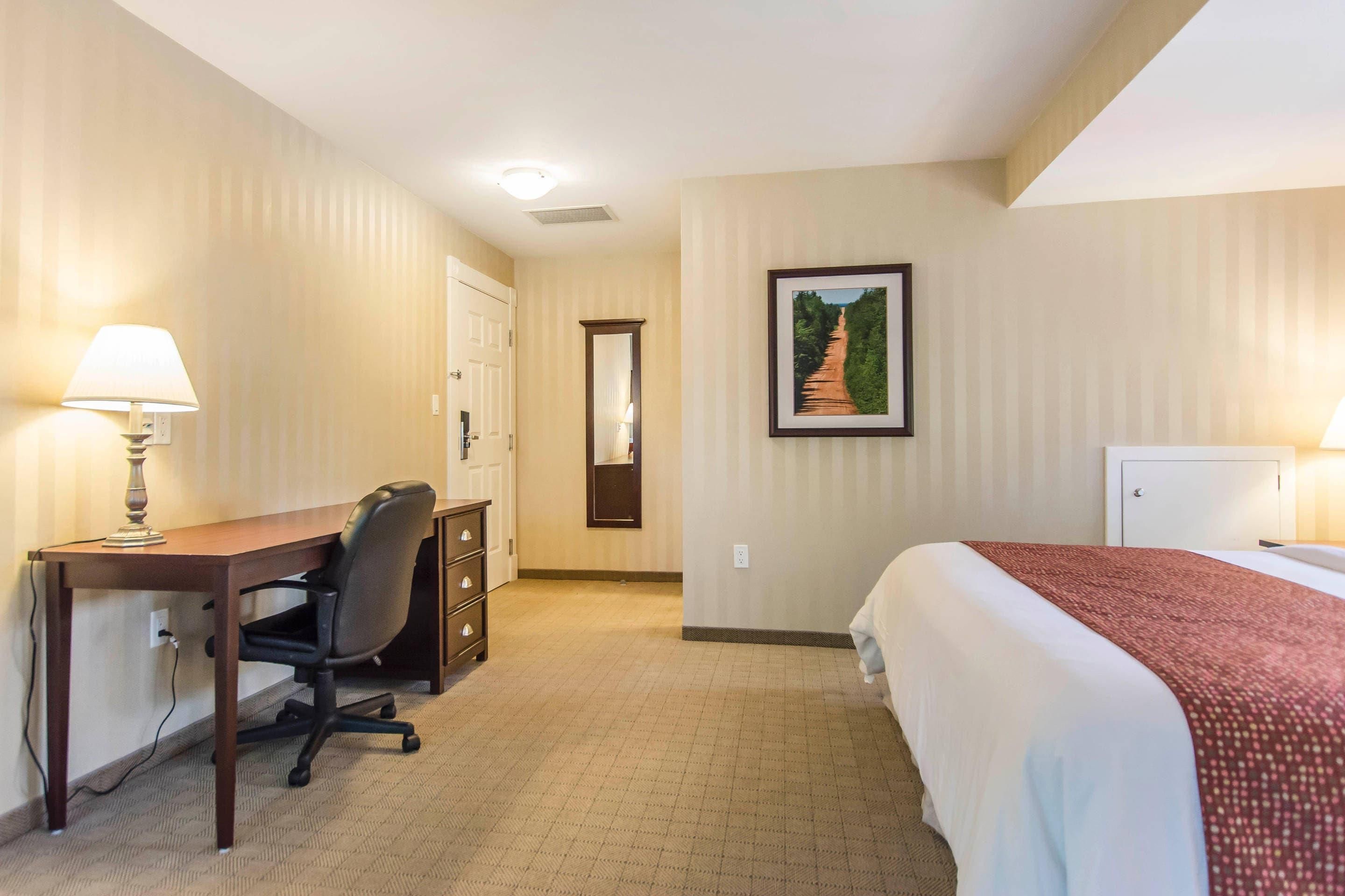 A hotel room with a bed, desk, chair, and a painting on the wall.