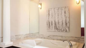A bathroom with a large bathtub, a mirror, and a wall-mounted artwork.