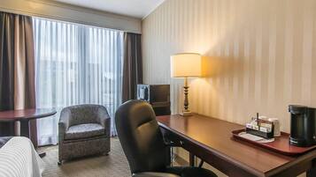 A hotel room with a bed, a desk with a lamp, a chair, a coffee maker, and a television.