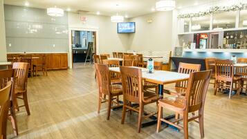 A spacious restaurant with wooden tables and chairs, a bar area, and a television mounted on the wall.