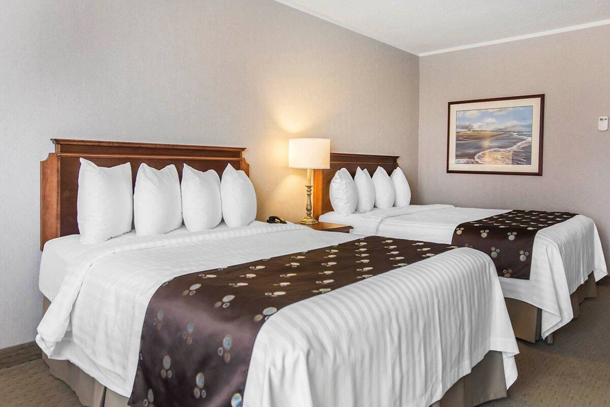 A hotel room with two beds, a nightstand with a lamp, and a framed picture on the wall.