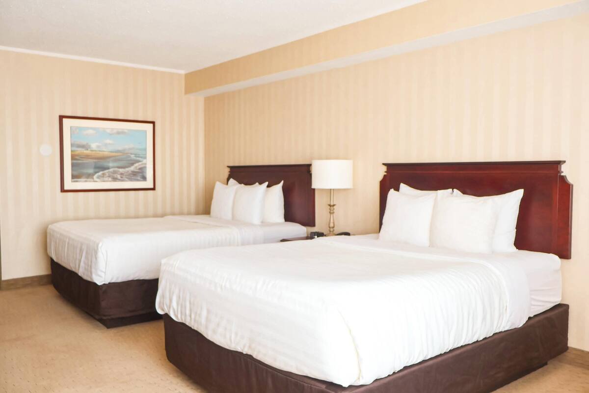 A hotel room with two beds, a nightstand, a lamp, and a framed picture on the wall.