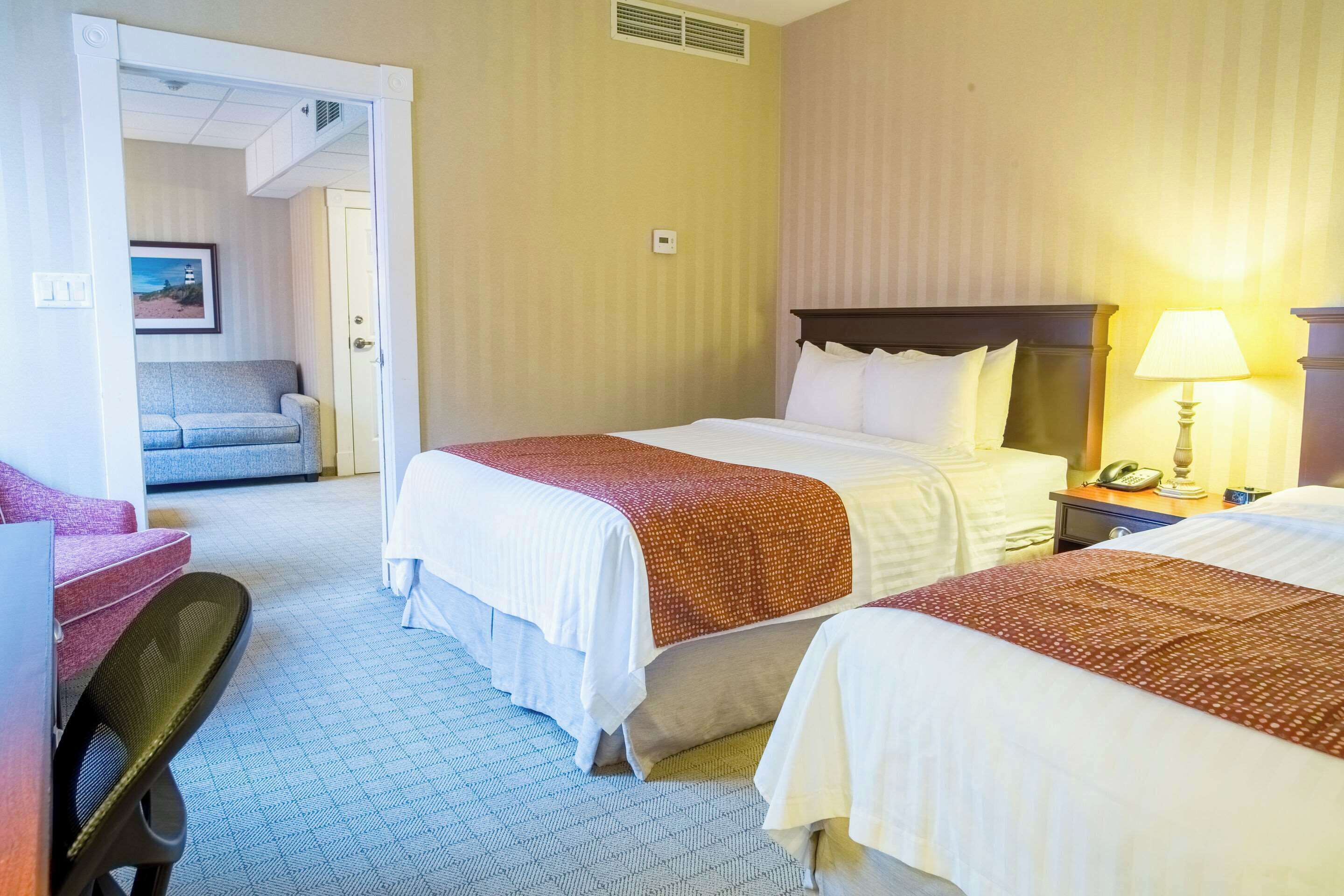 Une chambre d’hôtel avec deux lits, un bureau, une chaise, une table de chevet et une lampe.