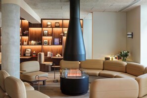 A modern lounge area with leather sofas, a central glass table with a fire feature, and a wooden bookshelf with various items. - Clubtrotteur Paris, a Tribute Portfolio Hotel (Paris)