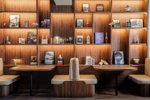 A hotel lobby with wooden paneling, two seating areas with cushioned chairs, and shelves with various items including books, decorative objects, and framed pictures. - Clubtrotteur Paris, a Tribute Portfolio Hotel (Paris)