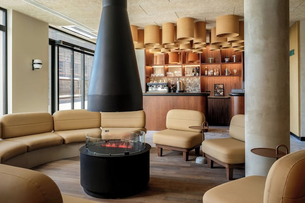 A modern lounge area with leather sofas, a central fire feature, and a bar area with wooden shelves. - Clubtrotteur Paris, a Tribute Portfolio Hotel (Paris)