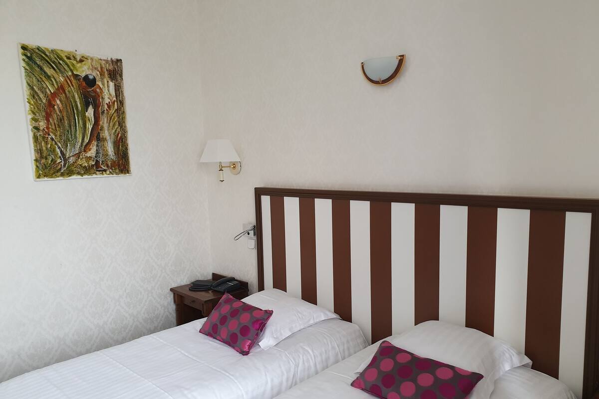 A hotel room with a bed, two pillows, a nightstand, a lamp, and a painting on the wall.