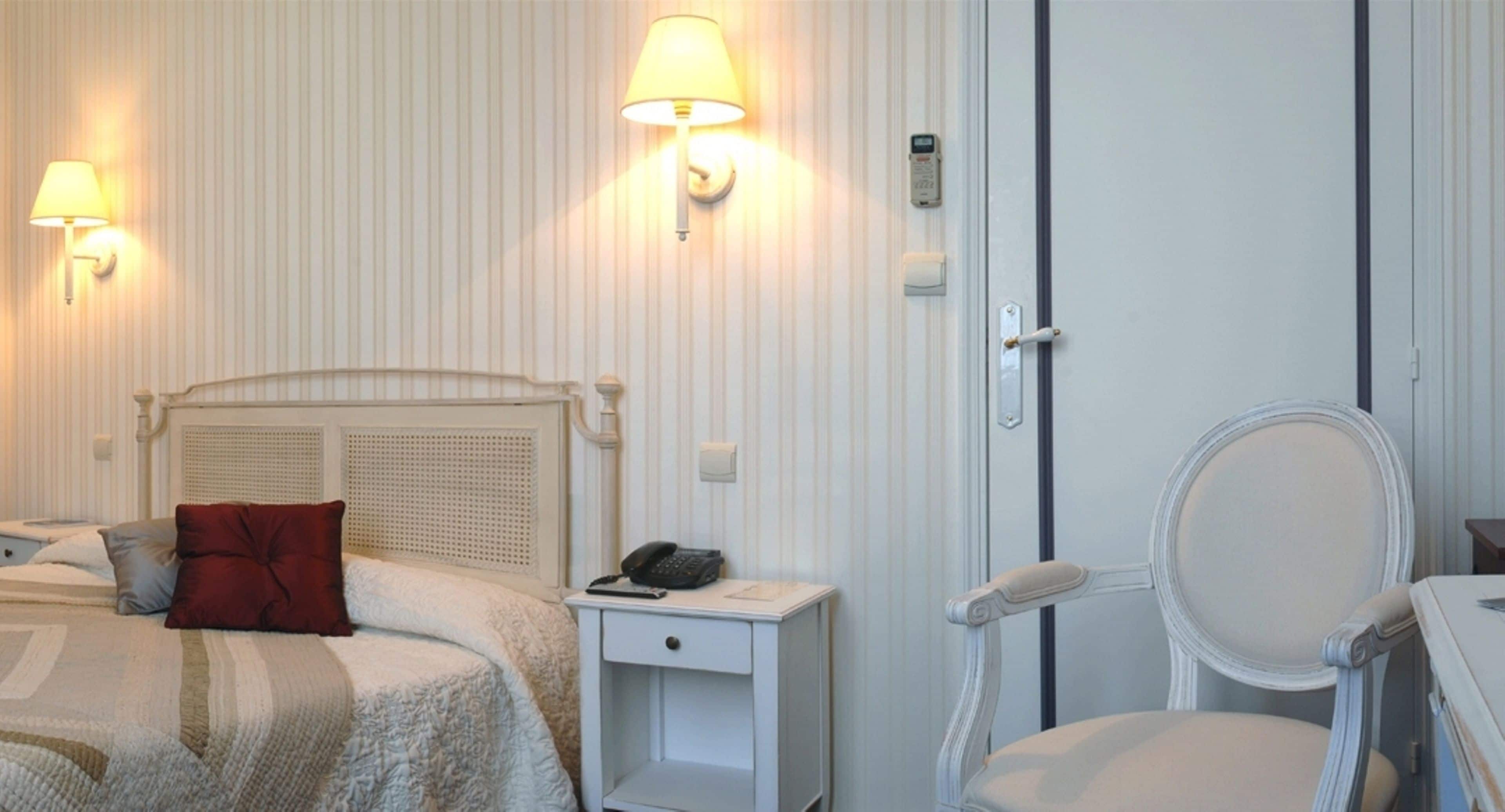 A hotel room with a bed, bedside lamp, nightstand, chair, and a door with a handle.