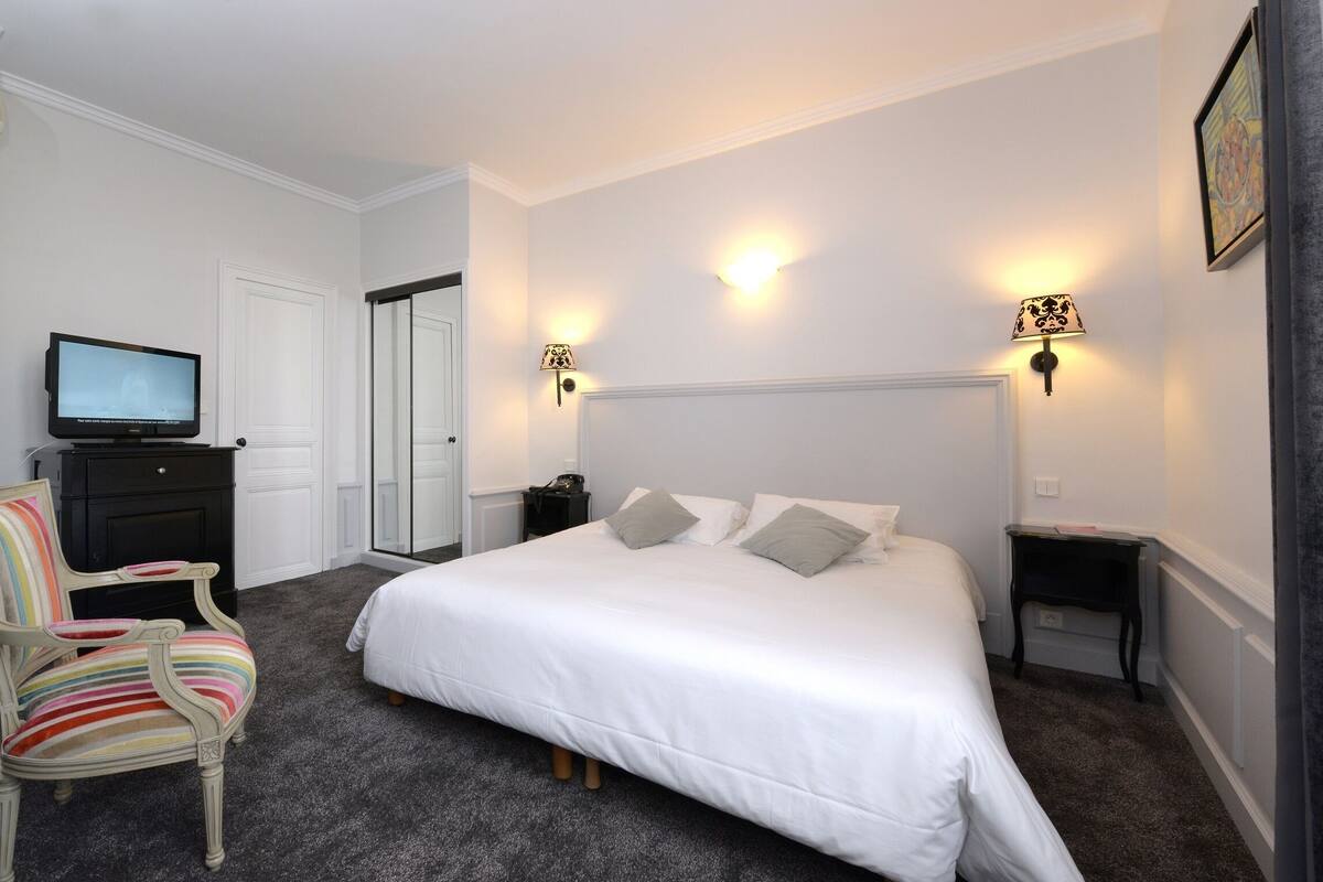A bedroom with a large bed, a television on a dresser, a chair, and two bedside tables with lamps.