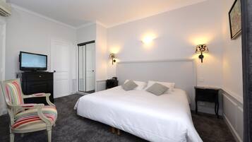 A bedroom with a large bed, a television on a dresser, a chair, and two bedside tables with lamps.