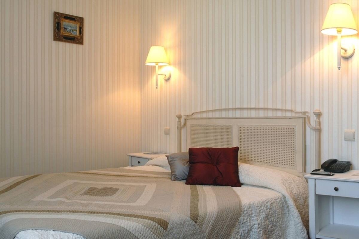 A hotel room with a bed, bedside tables, a mirror, and wall-mounted lamps.
