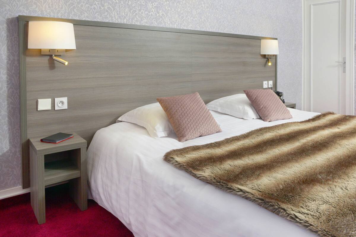 A neatly made bed with a fluffy brown throw blanket, two bedside lamps, and a small nightstand with a book.