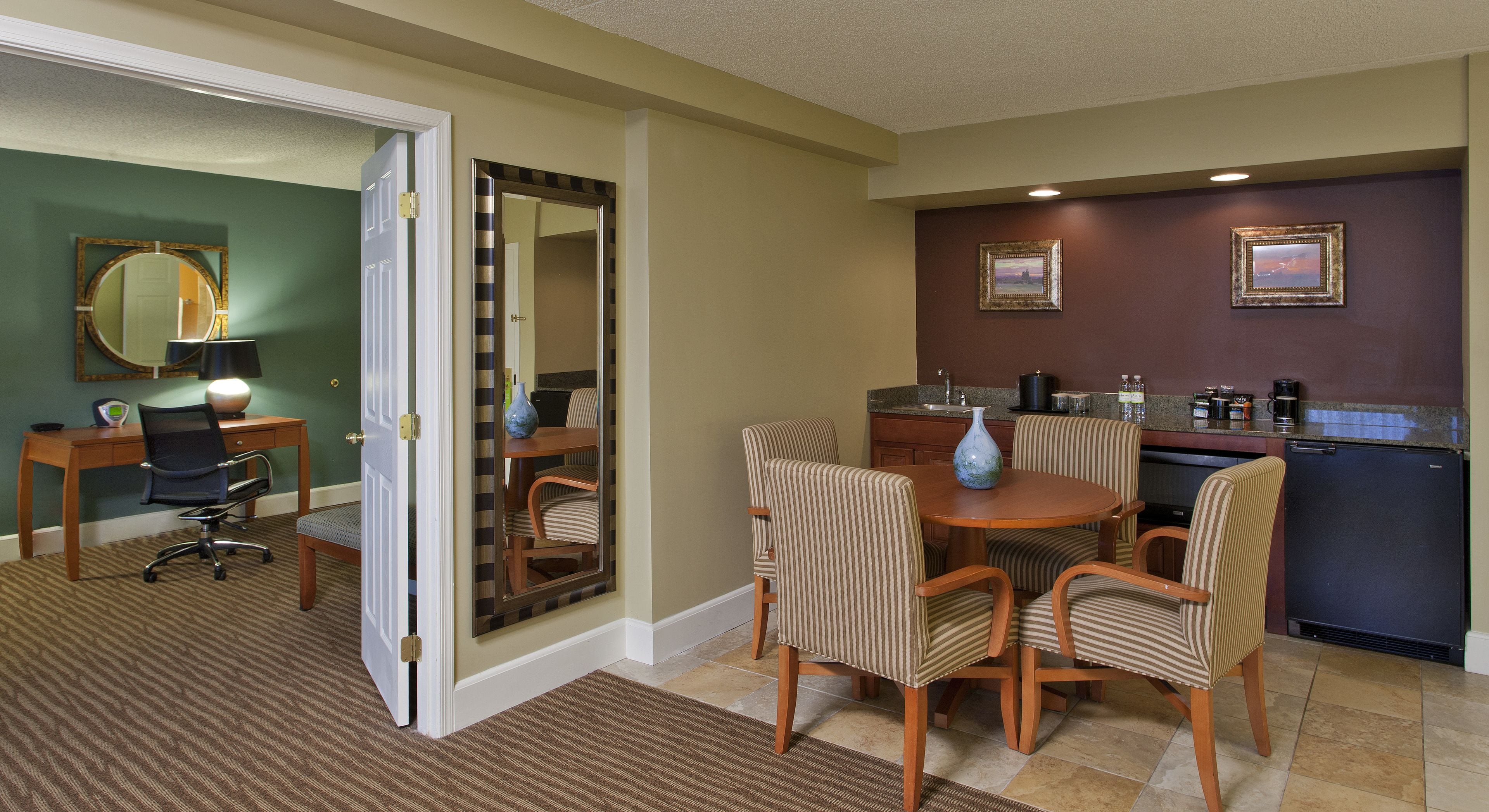A hotel room with a dining area, a kitchen, a bathroom, and a large mirror.