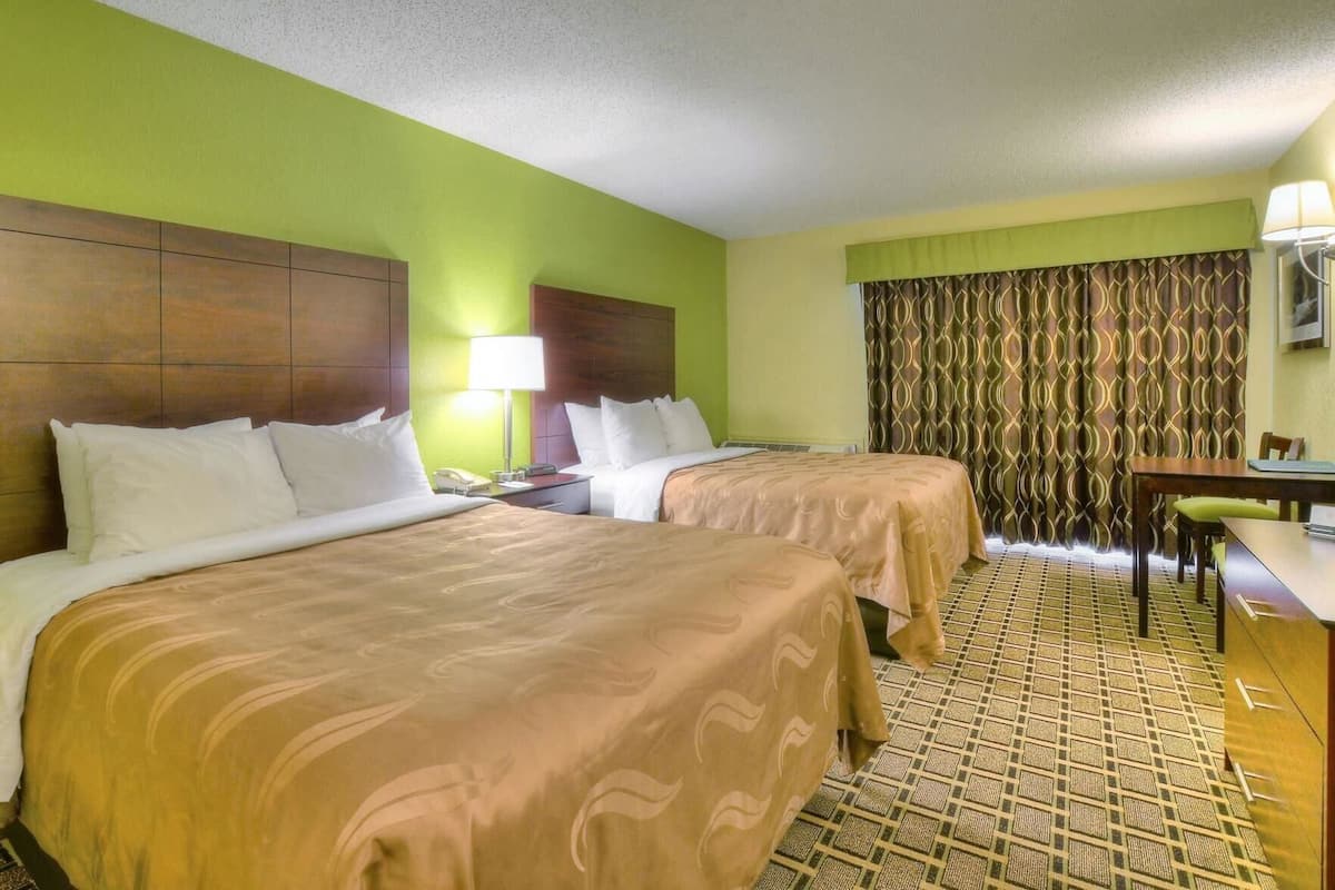 A hotel room with two beds, a desk, a chair, a lamp, and a patterned curtain.