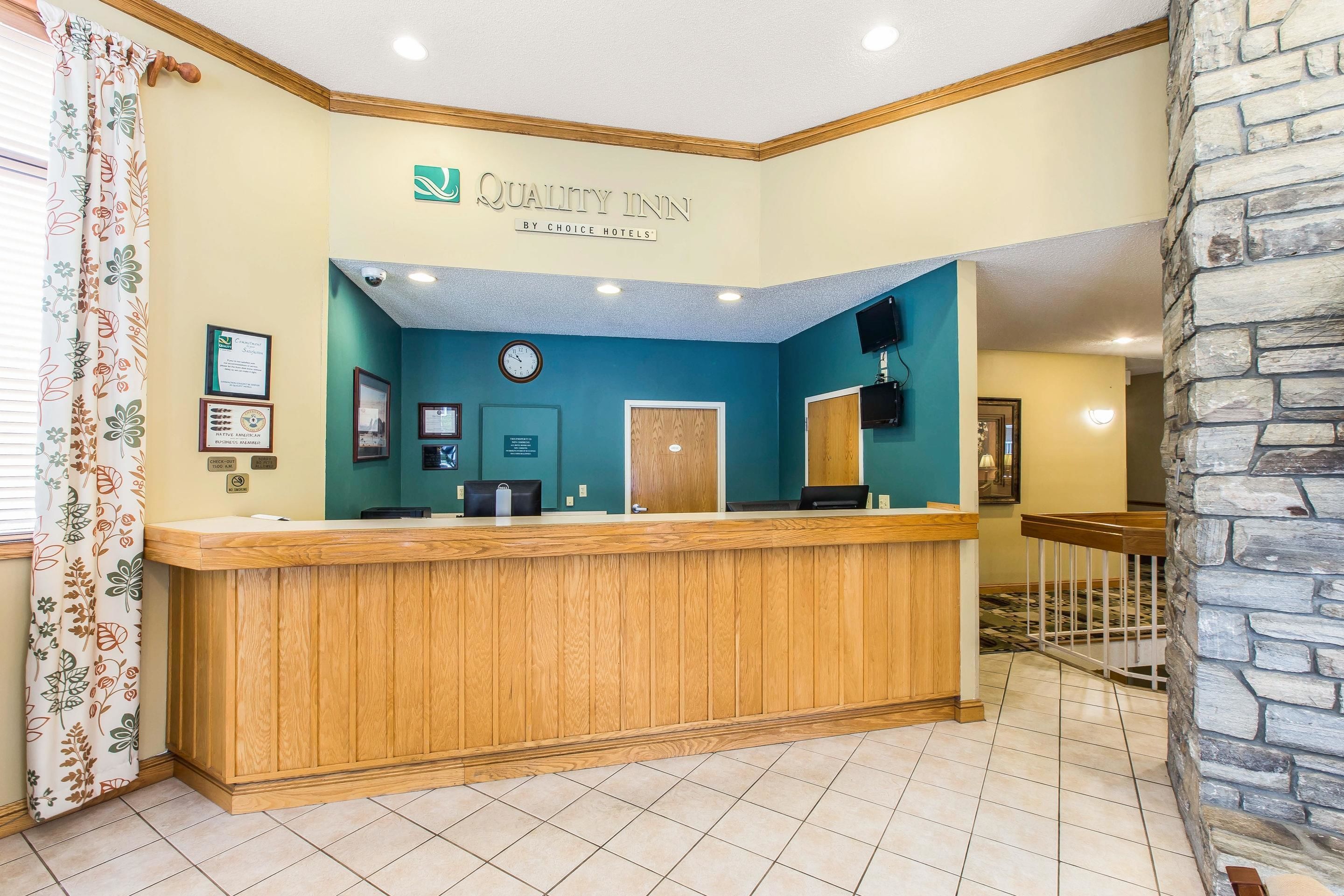 A reception area with a wooden counter, a clock, framed certificates, and a stone wall.
