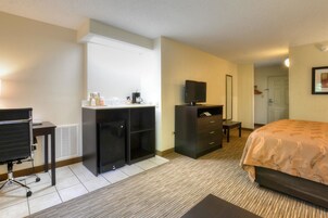 Habitación de hotel con cama, escritorio con silla, televisor, armario y una pequeña mesa con cafetera.
