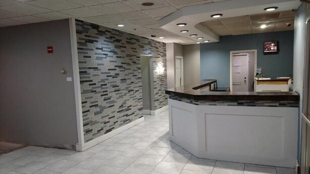 Un área de recepción con suelo de baldosas, mostrador con bancada, pared con diseño y una puerta al fondo.