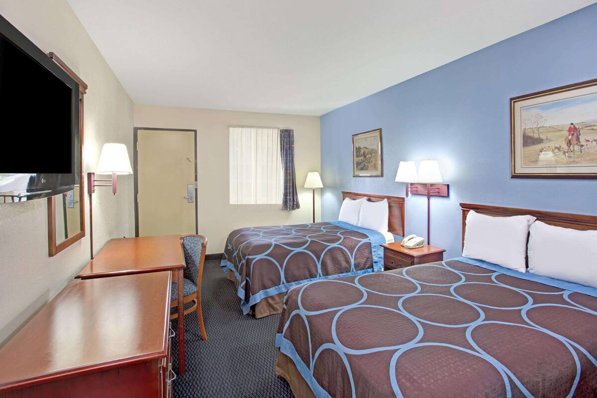 A hotel room with two beds, a desk, a chair, a TV, and a painting on the wall.