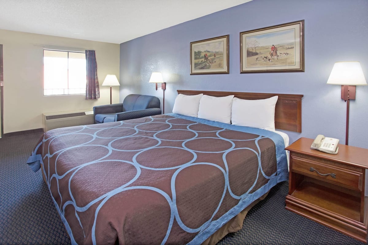A hotel room with a large bed, a desk with a phone, two wall-mounted lamps, and two framed pictures on the wall.