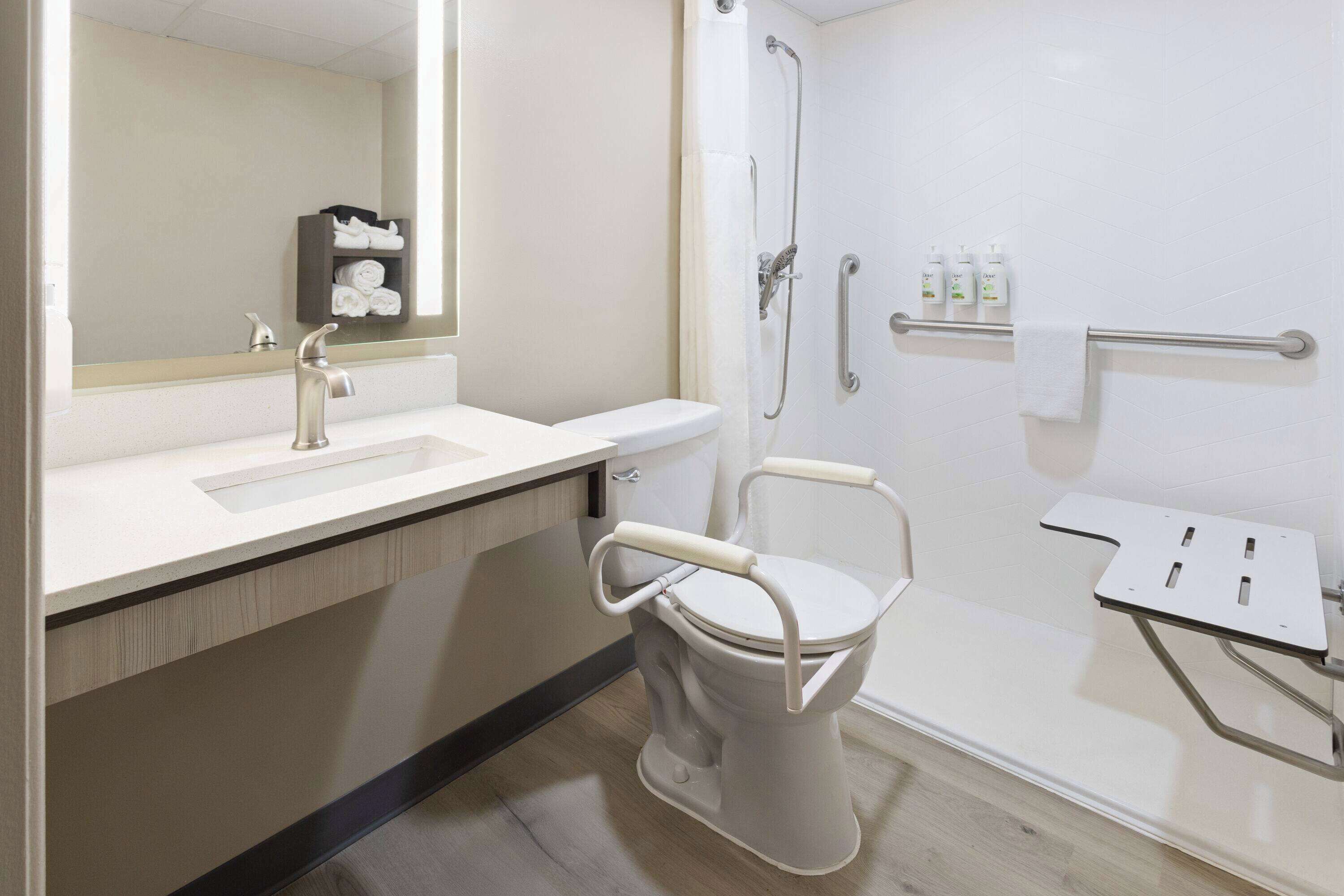 A modern bathroom with a white toilet, sink, and shower. There is a mirror above the sink, and a towel rack is visible on the wall.