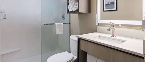 A modern bathroom with a glass-enclosed shower, a white toilet, a sink with a mirror above it, and a towel rack with towels.
