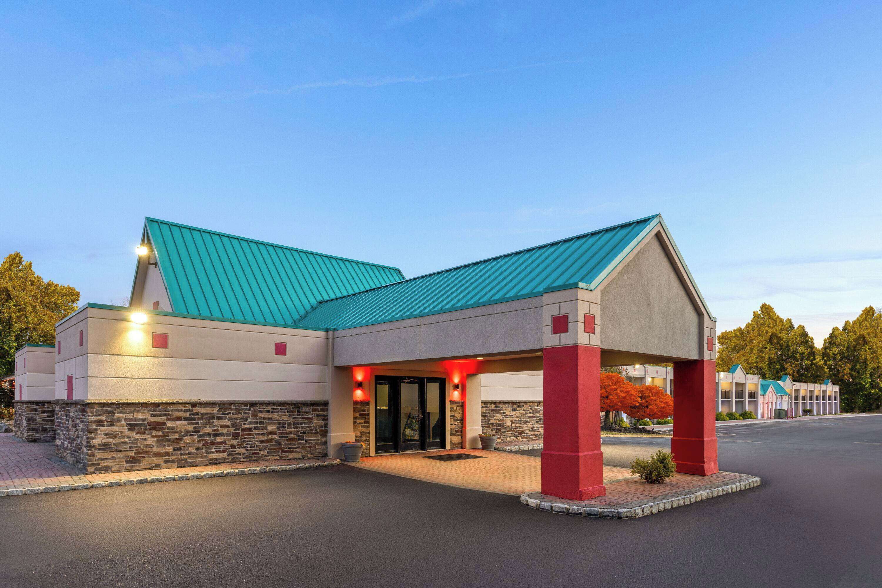 Un hotel con tejado verde, fachada de piedra y toldo de entrada rojo.