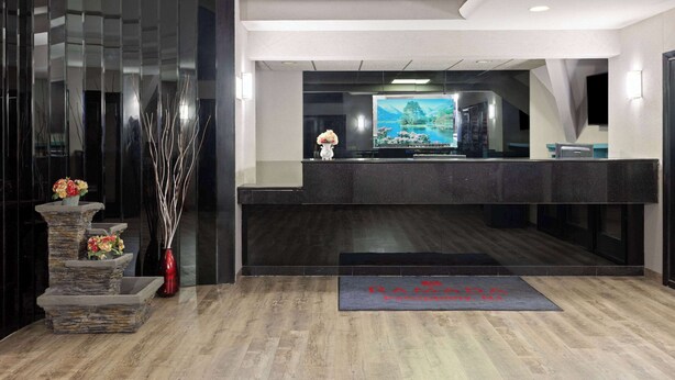 A reception area with a stone planter, a vase with flowers, and a welcome mat. - Ramada by Wyndham Parsippany (Parsippany)