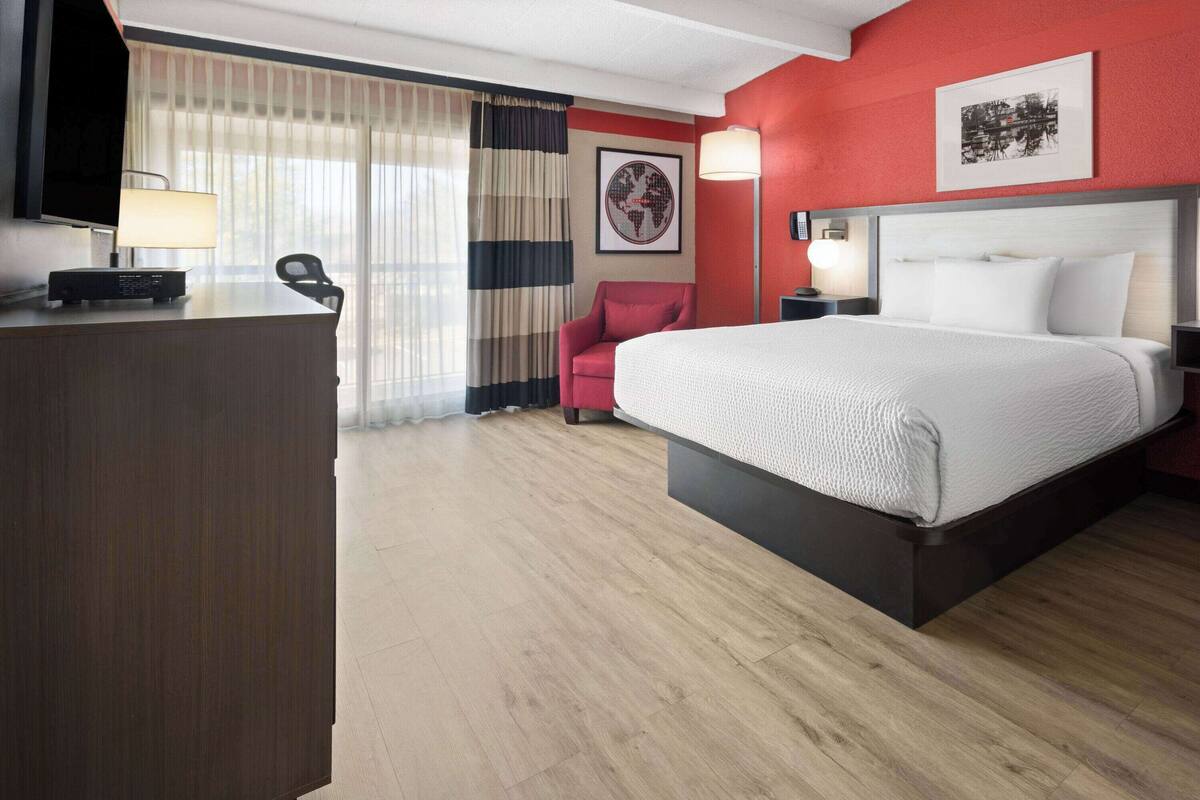 A hotel room with a bed, a desk with a lamp, a chair, and a TV.