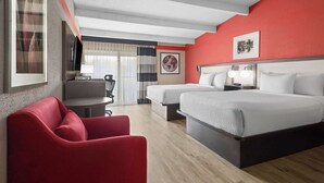 A hotel room with a red accent wall, two beds, a red armchair, a desk with a lamp, and a TV. - Ramada by Wyndham Parsippany (Parsippany)