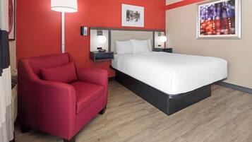 Una habitación de hotel con una pared roja, una cama blanca, un sillón rojo y una lámpara de pie.