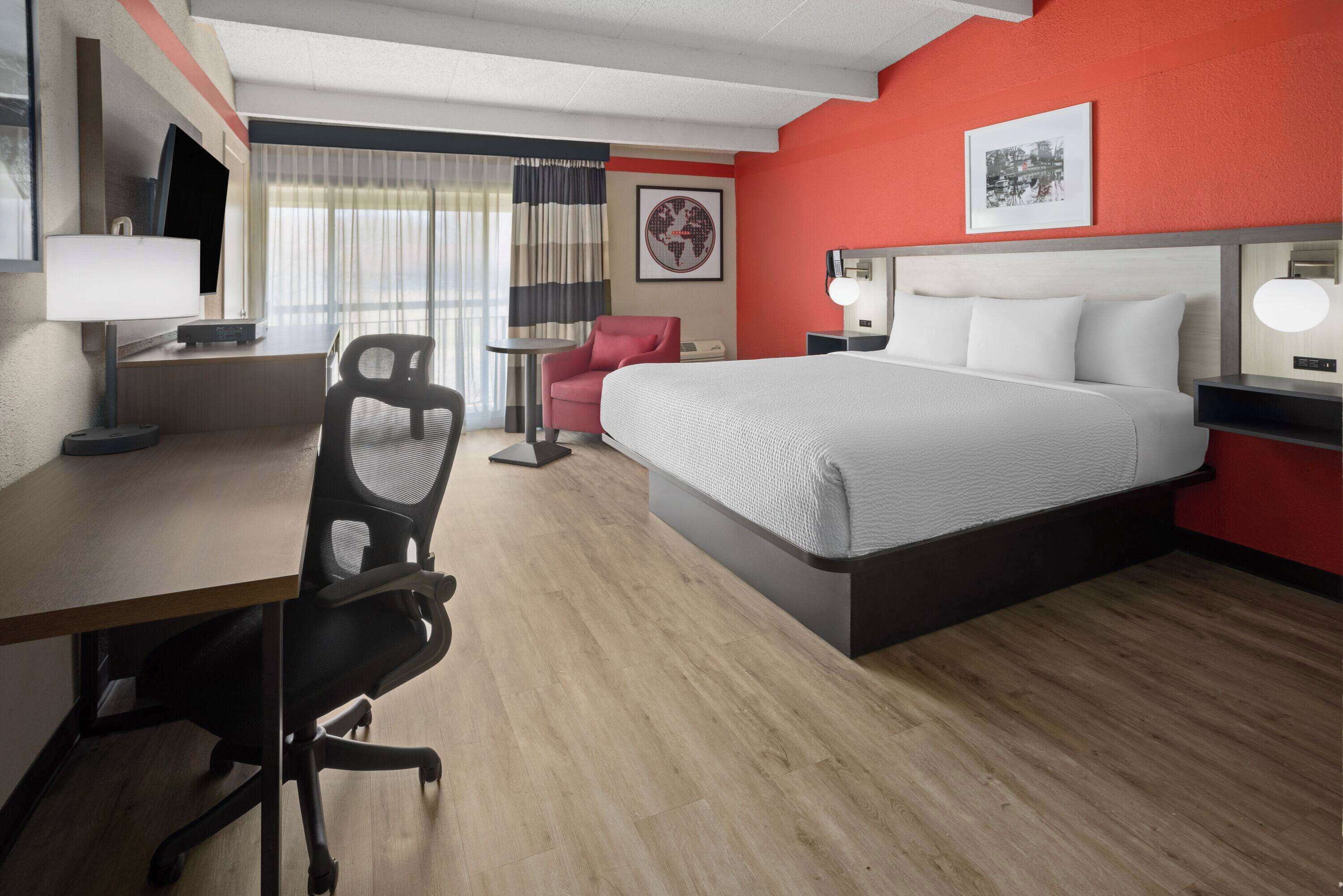 A hotel room with a bed, desk, chair, and a small table.