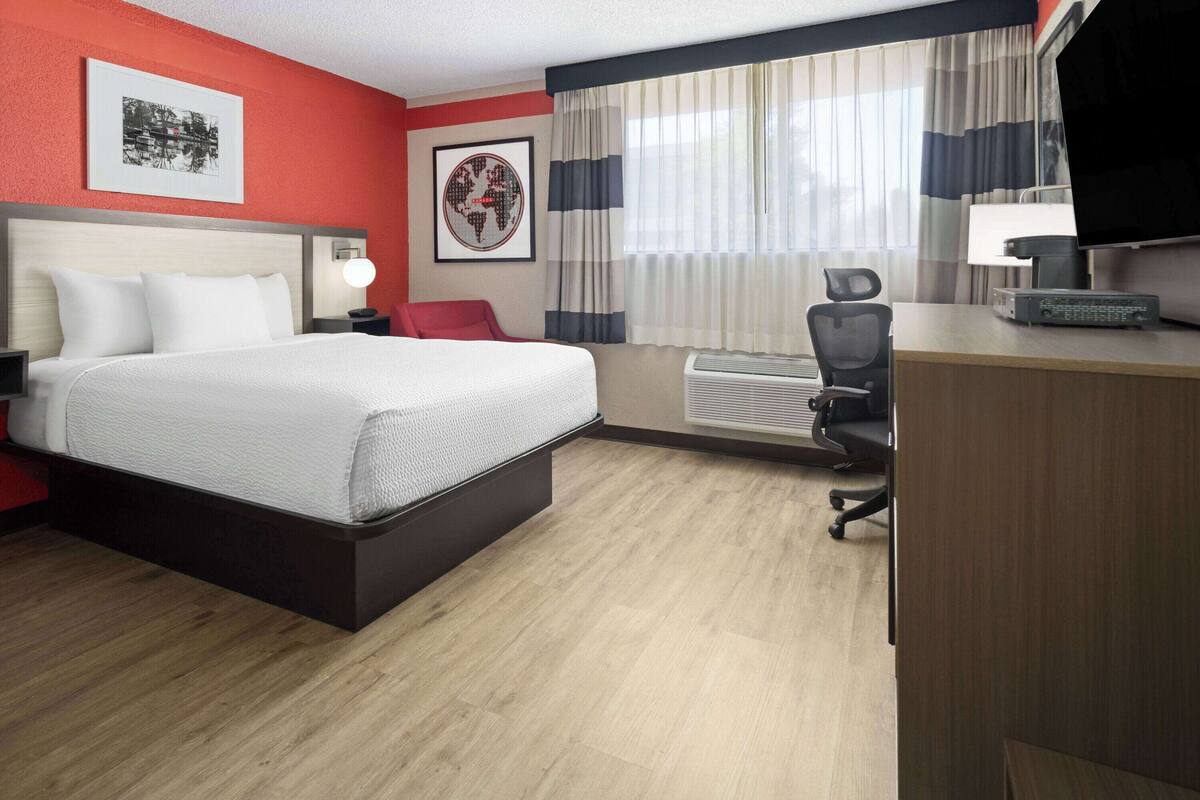 A hotel room with a bed, desk, chair, and a TV.
