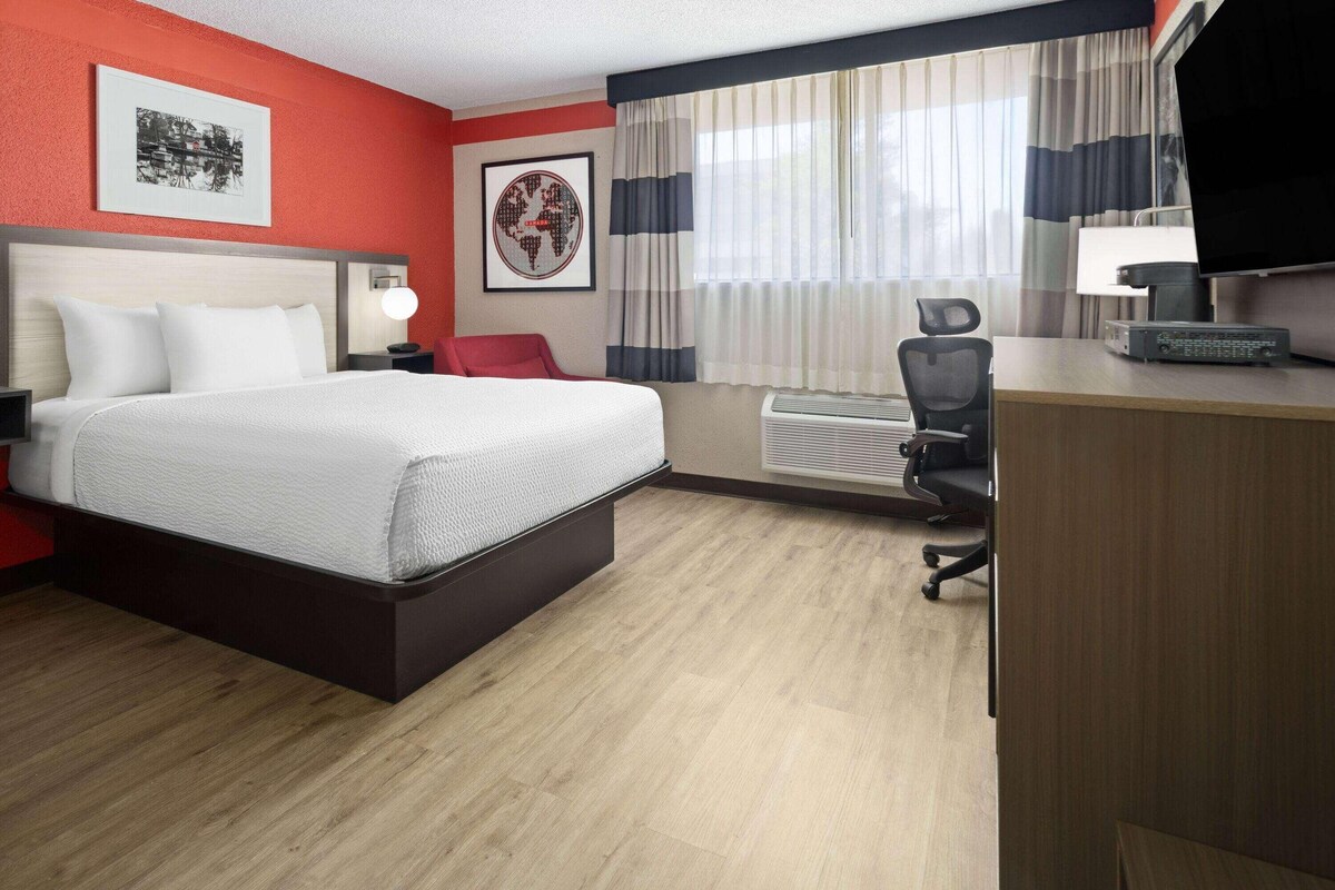A hotel room with a bed, desk, chair, and air conditioning unit.