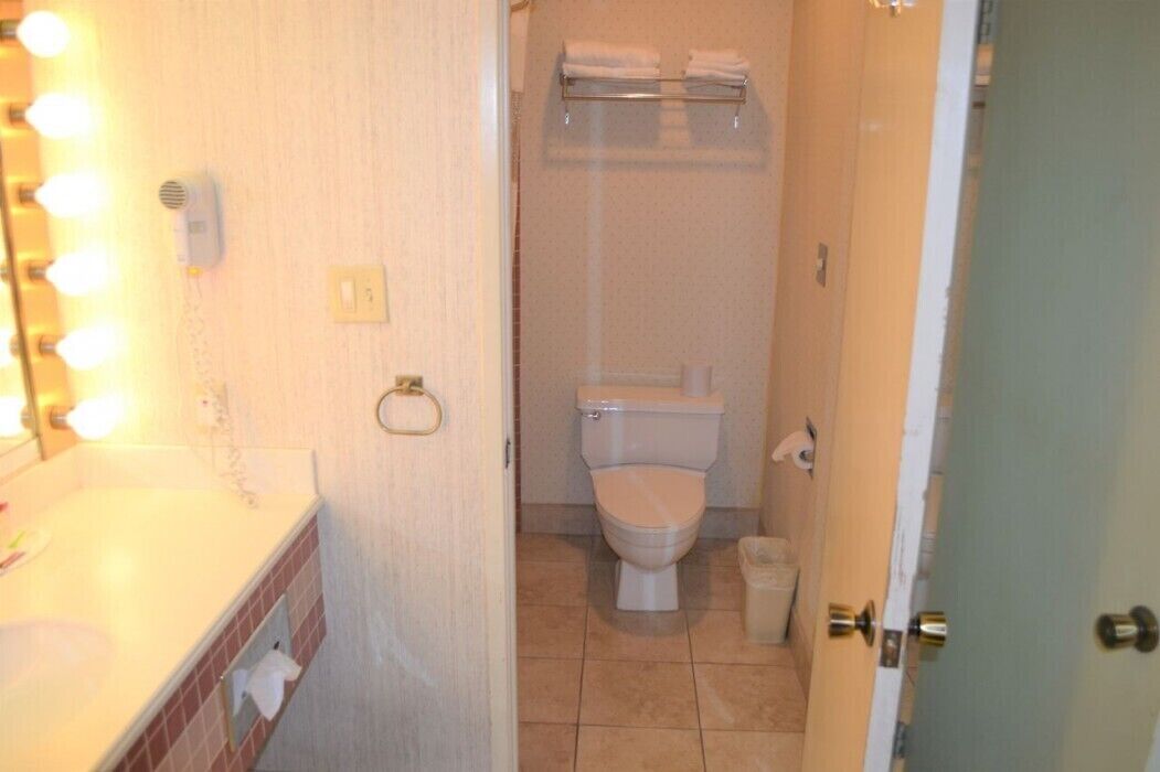 Un baño con lavamanos, espejo con luces, inodoro y perchero para toallas.