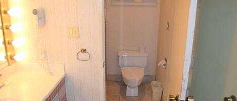 Un baño con lavamanos, espejo con luces, inodoro y perchero para toallas.