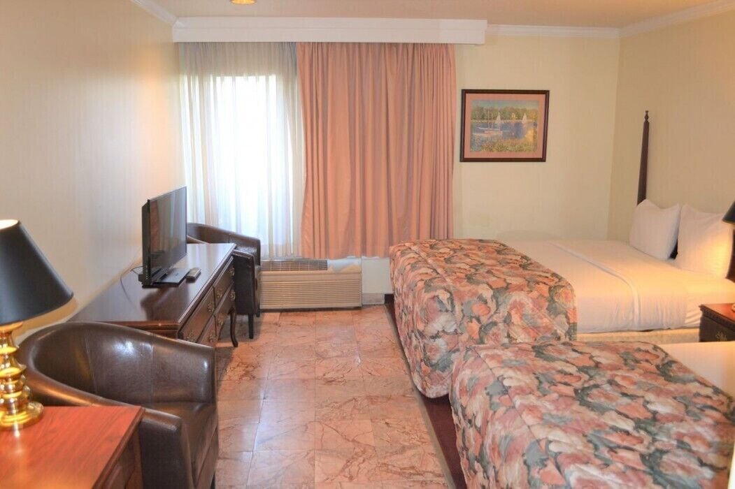 Une chambre d’hôtel avec un lit, un bureau avec une télévision, une chaise et une fenêtre avec des rideaux.